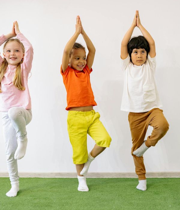 A child balancing on one leg in a tree yoga pose, smiling.